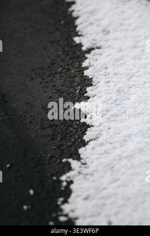 Close-up of fresh white snow resting on dark wet asphalt, creating a striking contrast between textures. Captured on a cold winter day in Latvia, high Stock Photo