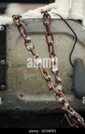 A close-up of a rusty chain covered with snow on an industrial surface in Latvia, capturing the contrast between the cold whiteness and the aged textu Stock Photo