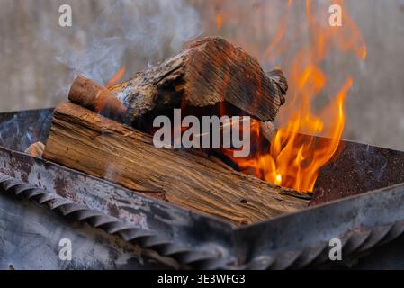 Close-up of wood burning in an outdoor barbecue grill, with vibrant flames and smoke, capturing the essence of a summer barbecue experience in a backy Stock Photo