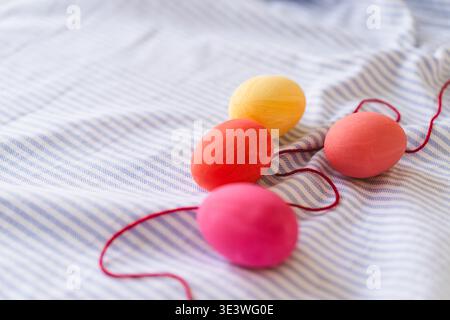 A vivid display of multicolored Easter eggs arranged on a light blue striped fabric. The eggs, in shades of pink, red, and yellow are connected by a r Stock Photo