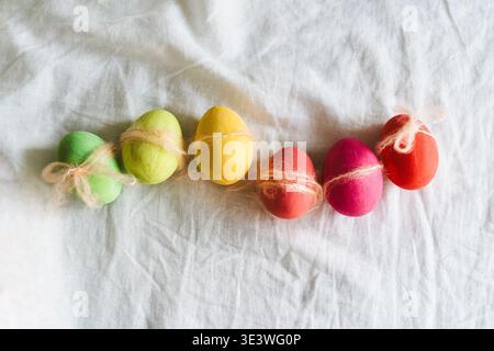 A festive arrangement of multicolored Easter eggs wrapped with natural twine, lying on a soft white cloth surface. The vibrant colors represent the jo Stock Photo