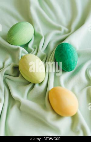 Multicolored Easter eggs lay elegantly on a soft green fabric, showcasing hues of green and yellow. These vibrant eggs symbolize the festive cheer of Stock Photo