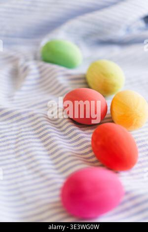 A collection of multicolored Easter eggs, featuring vibrant hues of pink, green, yellow and more, artistically arranged on a softly draped fabric back Stock Photo