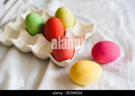 Multicolored Easter eggs displayed in an elegant egg tray on a soft, white cloth background. This vibrant collection of eggs embodies the festive spir Stock Photo