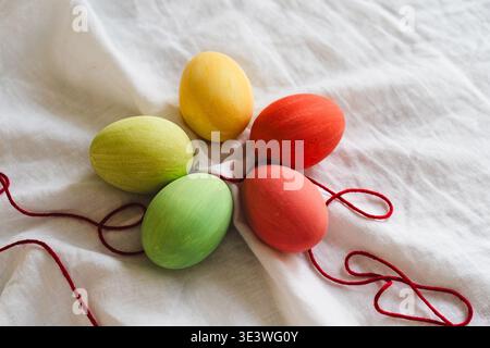 A vibrant display of multicolored Easter eggs on a soft white fabric, adorned with red string. This festive arrangement captures the joy and color of Stock Photo