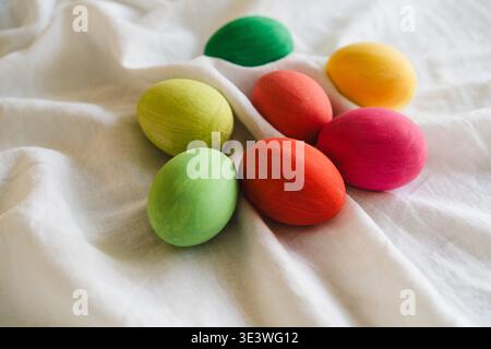 A collection of vibrant multicolored Easter eggs displayed on a soft white fabric, featuring shades of green, red, yellow and pink, embodying the fest Stock Photo