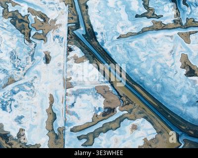 Aerial photograph capturing an abstract pattern in an icy landscape. Subtle hues of blue and brown compose an intricate design, resembling natural, fl Stock Photo