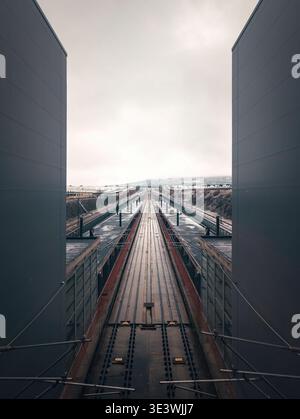 Symmetrical railway tracks stretch into the distance under a cloudy sky, flanked by industrial structures, portraying a dramatic and serene scene in S Stock Photo