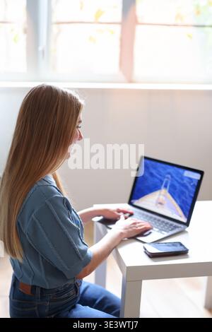 Young woman using laptop at home searching travel destinations online. Vacation planning and remote lifestyle concept. Stock Photo