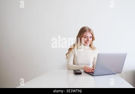 Young woman using laptop at desk. Freelance work, communication and productivity in modern home office. Stock Photo