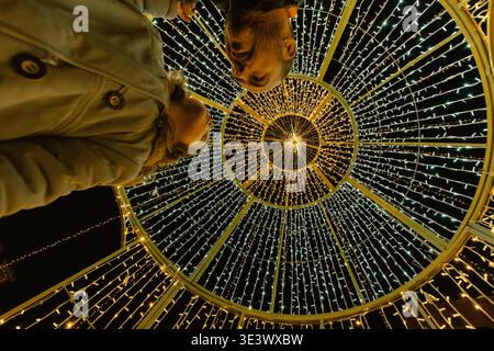 Low-angle shot of a father and his daughter under a large, illuminated Christmas tree in the spanish city of Astorga. Stock Photo