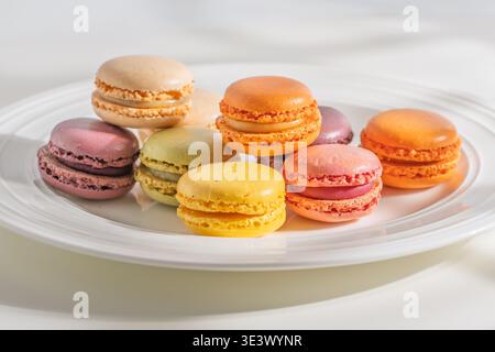 An assortment of colorful macarons is displayed on a white plate in natural light. Stock Photo