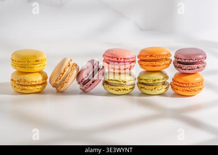 Pairs of colorful macarons are neatly lined up in a row under soft shadow patterns. Stock Photo