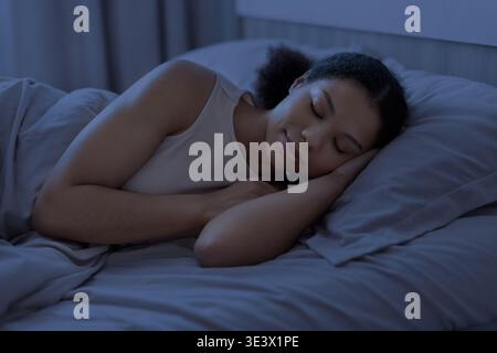 Young black woman sleeping peacefully in bed at night in cozy bedroom Stock Photo