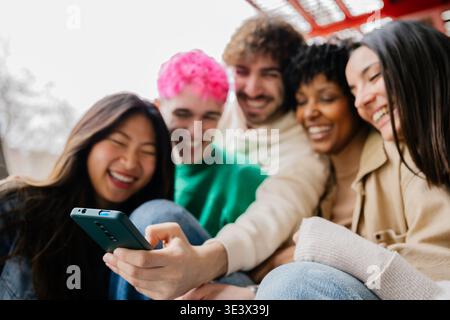 Diverse group of students sitting on campus stairs using phones together Stock Photo