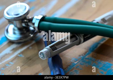 A professional medical stethoscope with green tubing lies next to an insulin pen with a sharp needle on a rustic wooden surface, symbolizing healthcar Stock Photo