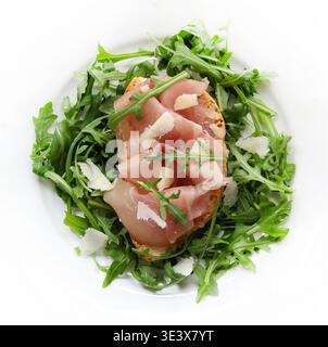 Bruschetta with prosciutto, fresh arugula, and parmesan shavings on a white background. A typical Italian dish. Stock Photo