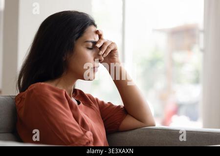 Overwhelmed young woman sitting alone indoors, close-up Stock Photo