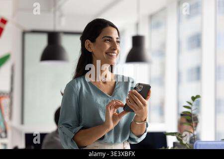 Smiling Brazilian female professional using mobile phone app at office Stock Photo