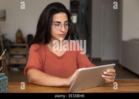 Serious Latina woman in glasses working on tablet device Stock Photo