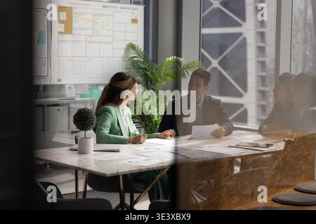 Female project manager discussing documents with diverse associates around table Stock Photo