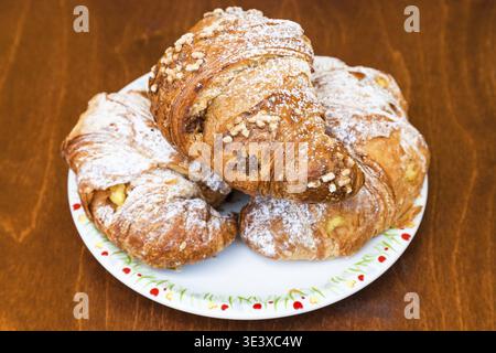 Three fresh Italian croissants filled with vanilla and chocolate creams on a wooden table Stock Photo