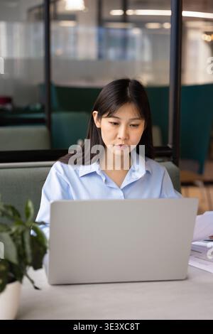 Focused East Asian office employee working on laptop in coworking Stock Photo