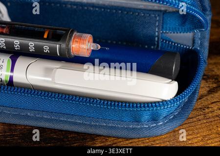 Insulin pen with drug drop on needle tip in a blue case on a wooden table. Medical injection equipment for diabetes management and treatment. Stock Photo