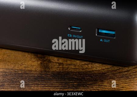 Close-up of USB-C and USB-A charging ports on a dark grey power bank. Labels C3 IN OUT and A OUT are clearly visible in blue text. The device sits on Stock Photo