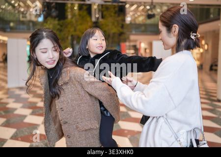 Three women laugh together in a modern shopping mall. One playfully pushes another as they share a joyful moment. The atmosphere feels light, carefree Stock Photo