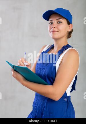 Young woman in work overalls making notes Stock Photo