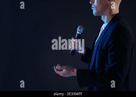 Presenter with microphone performing on dark background, closeup. Space for text Stock Photo