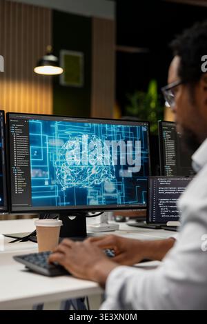 Engineer utilizing AI on computer to optimize performance and forecast issues. African american worker in tech company office training machine learning models to perform automatic updates Stock Photo
