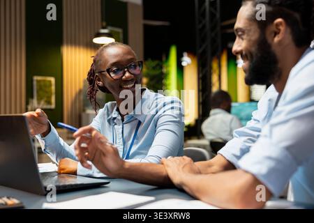 Discussing project ideas, fun and happy employees in relaxed coworking space. collaborating, pleasant chat and jolly multiethnic coworkers at office desk finishing work tasks Stock Photo