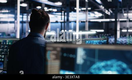 Server room software developer using AI to review infrastructure diagnostics. IT employee in data center analyzing performance data using artificial intelligence technology on devices, camera A Stock Photo
