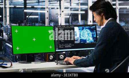 Data center programmer using green screen PC monitor, using AI. Man in tech startup office using artificial intelligence on chroma key computer to oversee servers powering deep learning, camera A Stock Photo