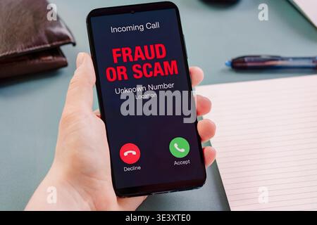 Person holds smartphone showing incoming scam call alert on screen, highlighting fraud risk, cyber threat awareness, mobile security issue, digital sa Stock Photo