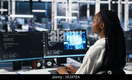 Female programmer in data center reviews AI diagnostics, analyzing neural network performance. Server hub IT expert optimizes artificial intelligence systems configuration, camera A Stock Photo