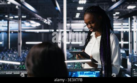 Technicians in high tech data center cooperate on neural network software development. Server hub IT workers talking, implementing deep learning technology using PC, camera A Stock Photo