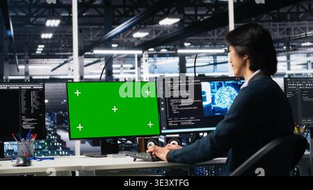 Data center technician managing AI systems using mockup PC. IT professional in tech startup office using artificial intelligence on green screen computer in server hub, camera A Stock Photo