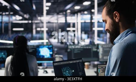 Data center programmer using laptop to monitor neural network using AI LLM chatbot. Worker using artificial intelligence on notebook to oversee servers powering machine learning, camera A Stock Photo