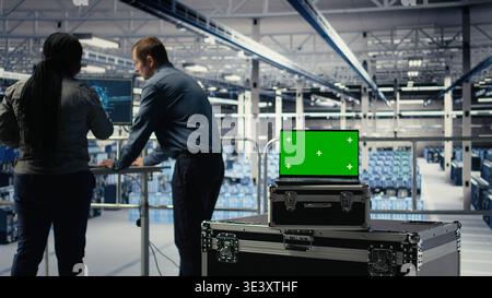 Close up of isolated screen laptop in front of data center programmers improving AI rigs processing speed. Server hub coworkers manage gear using chroma key device to support AI workloads, camera A Stock Photo