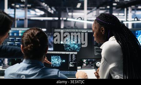 Teamworking data center technicians using machine learning algorithms to analyze large datasets. Server room colleagues gathered together at desk, collaborating, using AI neural networks, camera A Stock Photo