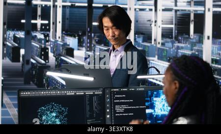 Software developers cooperating in data center, reviewing AI diagnostics on computer. IT staff members discussing in server room, optimizing machine learning systems, camera A Stock Photo