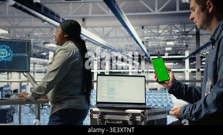 Server room software developer using mockup phone while waiting for updates to finish installing. Data center engineer uses green screen smartphone, waiting for code to finish compiling, camera A Stock Photo