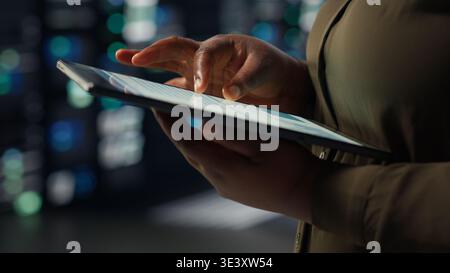 Close up of technician working in data center using tablet to optimize network infrastructure. IT expert in server farm diagnosing and resolving hardware malfunctions using device Stock Photo