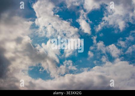 Fluffy, vibrant cumulus clouds float across a bright blue expanse. A serene, airy atmosphere fills the sky, showcasing nature's beauty Stock Photo