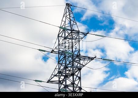 Massive electricity pylon dominates the frame, its robust steel structure against a dynamic sky. Power lines stretch across a cloudy backdrop Stock Photo