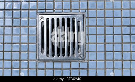 Metal drain embedded in a floor of blue square tiles Stock Photo