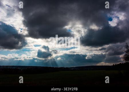 Dramatic sky with powerful, moody clouds and striking sun rays breaking through. A dark landscape silhouette completes this intense, atmospheric scene Stock Photo